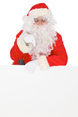 Naklejka premium Santa Claus pointing on blank white wall, advertisement banner with copy space. Isolated on white background
