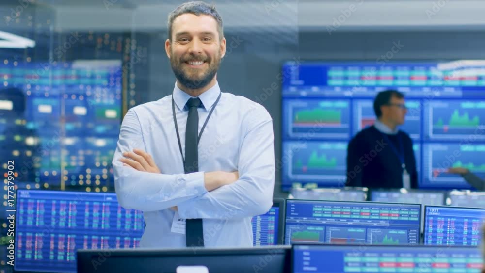 Poster successful male stock trader crosses arms and smiles at the camera. in the background busy stock exc