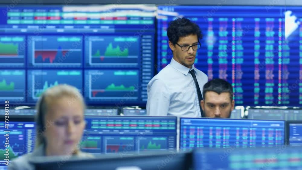 Poster Stock Trader Enters Office and Shakes Hands with a Colleague, Makes Work Related Chat with Other. Busy Office with Multi-Ethnic Team of Brokers, Dealers. Displays Show Numbers and Infographics.