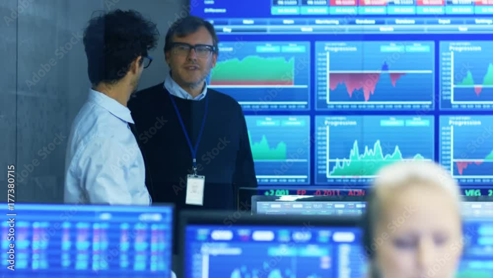 Poster Stock Trader Enters Office and Shakes Hands with a Colleague, Makes Work Related Chat with Other. Busy Office with Multi-Ethnic Team of Brokers, Dealers. Displays Show Numbers and Infographics.