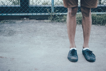 A man legs wearing black canvas shoes and brown pants standing on concrete ground with copy space in Japanese tone style. Fashion divided into shorts sneakers.