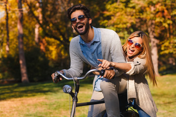 Happy young couple having fun riding a bicycle on sunny autumn day in the park.