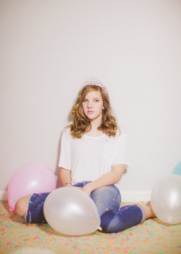 Teen girl wearing a tiara with confetti and balloons around her