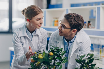 happy biologists in white coats with lemon plants in laboratory