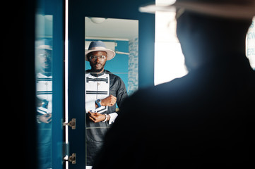 Rich african man looking at mirror on wardrobe at his appartment. Portrait of successful black man indoor.