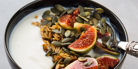 Healthy breakfast natural yogurt bowl with home made granola, pumpkin seeds and figs on gray background