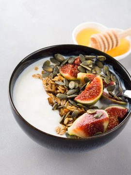 Healthy breakfast natural yogurt bowl with home made granola, pumpkin seeds and figs on gray background