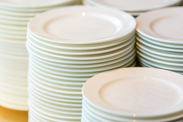 Stacks of cleaned white plates for catering buffet in restaurant room