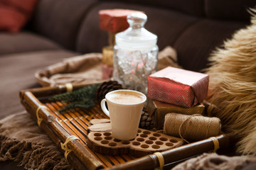 Christmas lifestyle concept.. Cup of coffee on tray, gifts, cones and plaid of living room. Christmas home decoration.