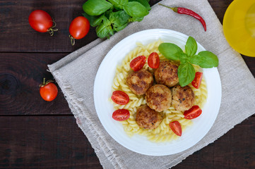 Pasta futsilli with meat balls, cherry tomatoes, basil on a white plate on a dark wooden background. Top view.