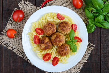 Pasta futsilli with meat balls, cherry tomatoes, basil on a white plate on a dark wooden background. Top view.