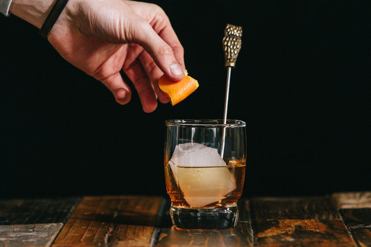 Man's hand holding orange peel at old fashioned drink