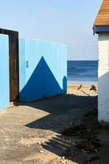Blue hut on a beach with sharp shadow and ocean