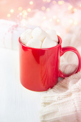 Red Mug with Hot Chocolate Cocoa Drink and Marshmallows on Top. Glittering Sparkling Garland Lights in Background. Knitted Sweater Gift Box. Soft Pastel Colors. Christmas New Year Romantic Cozy