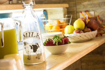 Countertop with a bottle of milk,a  jar with colorful juice and containers with strawberries, apples and oranges. Concept of healthy breakfast