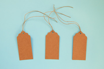 Three brown blank paper price tags or labels set on the blue background, top view.