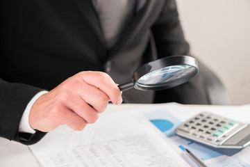 Businessman reading documents with magnifying glass concept for analyzing a finance