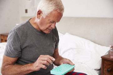 Senior Man Sitting On Bed At Home Taking Medication