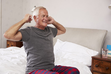 Senior Man Waking Up And Stretching In Bedroom