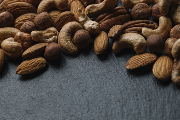 Variety of mixed nuts - almond, hazelnuts and cashew - on the dark slate background with copy space. Top view. Toned
