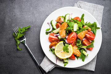 Fresh salad with salmon and vegetables on black background.