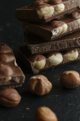 Chocolate bar pieces and nuts on dark background with copy space. Chocolate background. Toned