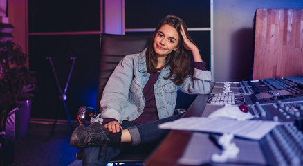 Female music composer sitting by sound mixing console - obrazy, fototapety, plakaty