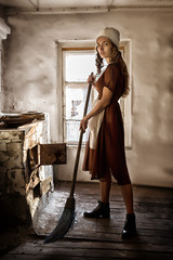 woman in a rustic dress sweeps the wooden floor in the kitchen