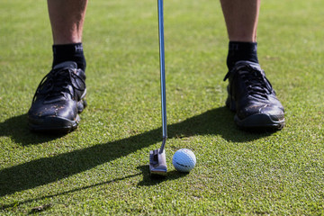 Obraz premium Putting a golf ball with a putter black shoes