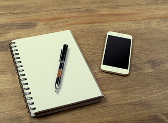 Smartphone with notebook and pen on wooden table. Office.