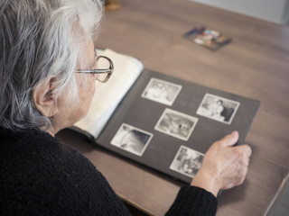 Fototapeta na wymiar Elderly woman looking through old photographs. Shot from behind