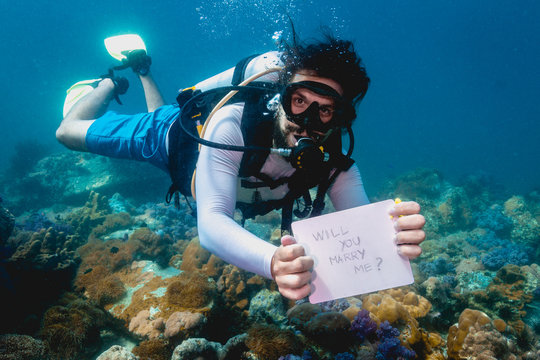 Scuba diver holding  Will you marry me? sign making unusual underwater marriage proposal