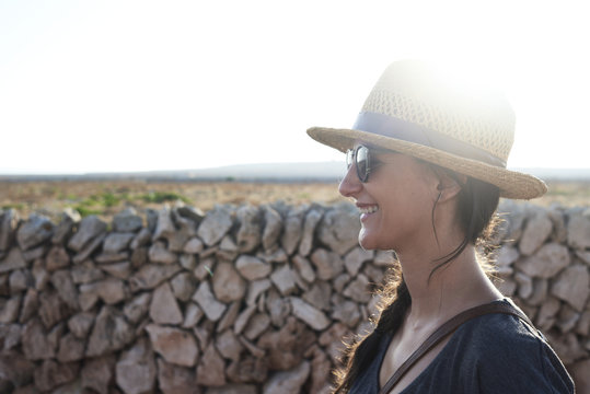 Spain, Menorca, happy single traveler wearing straw hat and sunglasses at backlight