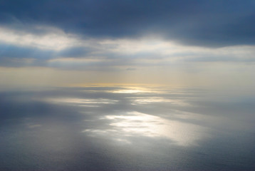 Naklejka na ściany i meble Sun shining at open sea through clouds making reflections at sea surface. Shot from airplane.