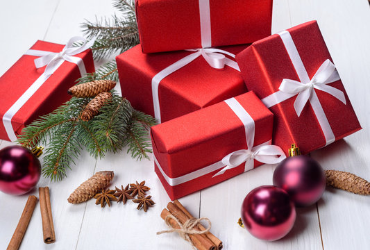 Christmas background with red gift boxes, fir tree branches, pine cones, glass balls, cinnamon sticks and star anise. Red gift boxes on white wooden background. Holiday greeting card