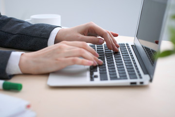 Close-up of business woman  hands  typing on  laptop computer in the white colored office.