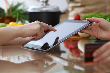 Close-up of human hands pointing into tablet  in the kitchen. Friends having fun while choosing menu or making online shopping.  Cooking, healthy meal and friendship concept