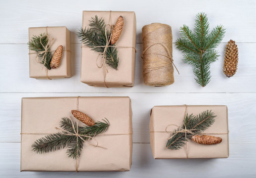Christmas background with gift boxes wrapped in kraft paper with fir tree branches and cones on white wooden background, free space. Holiday greeting card, copy space. Flat lay, top view