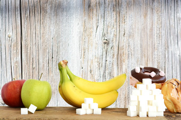 Analyzing the quantity of sugar in different foods, suggested by piles of sugar cubes in front of fruits and desserts on wooden background