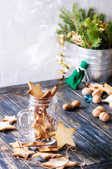 Homemade shortbread star shape sugar cookies different size in glass jar and as garland on old wooden table decorated by Christmas tree and gifts. Christmas mood theme.