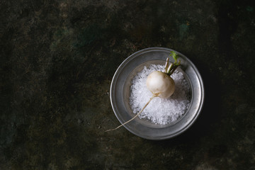 Whole white fresh organic radish in metal plate with sea salt over dark metal texture background. Top view with copy space. Vegetarian concept