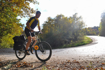 Naklejka premium Traveler rides a bicycle along a winding mountain road. Cyclist on the road on sunny autumn day