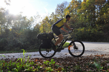 Traveler rides a bicycle along a winding mountain road. Cyclist on the road on sunny autumn day