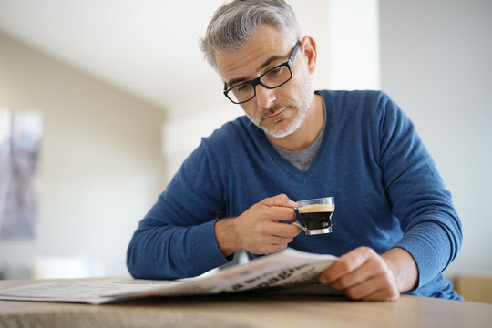 Middle-aged man at home drinking coffee and reading newspaper