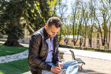 Obraz premium A man sitting in the park looks at his mobile phone