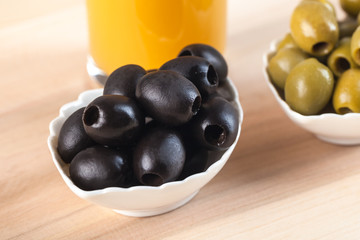 White bowl with green olives on wooden table