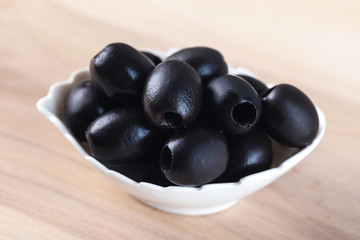 White bowl with black olives on wooden table
