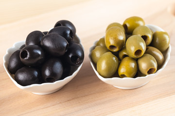 White bowl with green olives on wooden table