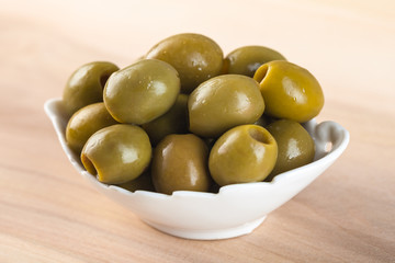 White bowl with green olives on wooden table