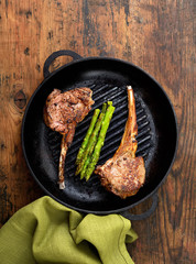 grilled lamb steak with asparagus in a frying pan on a wooden background